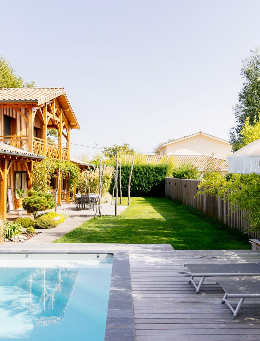 Vue sur une villa en bois à Lège-Cap-Ferret, avec piscine et terrasse équipée de transats.