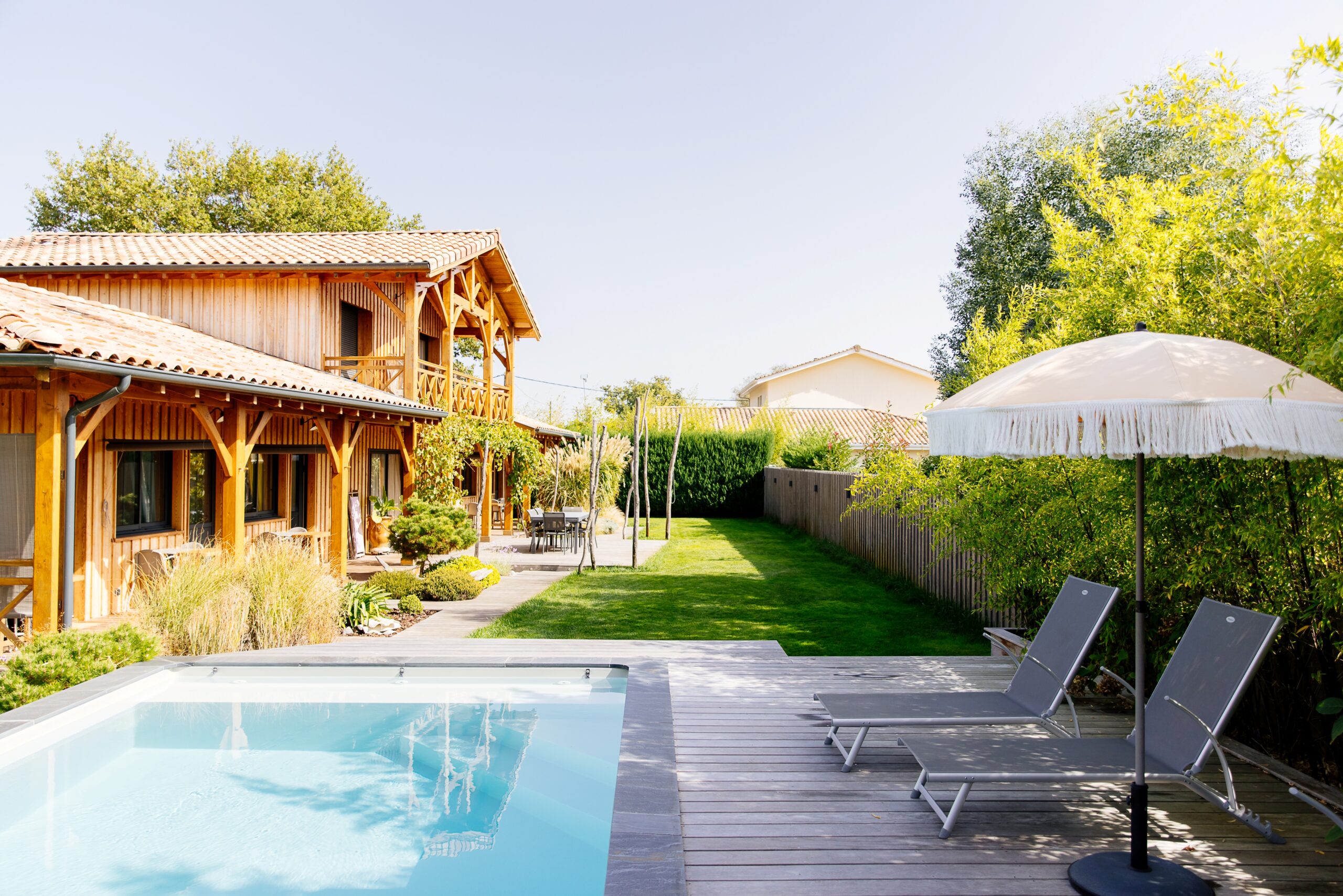 Vue sur une villa en bois à Lège-Cap-Ferret, avec piscine et terrasse équipée de transats.