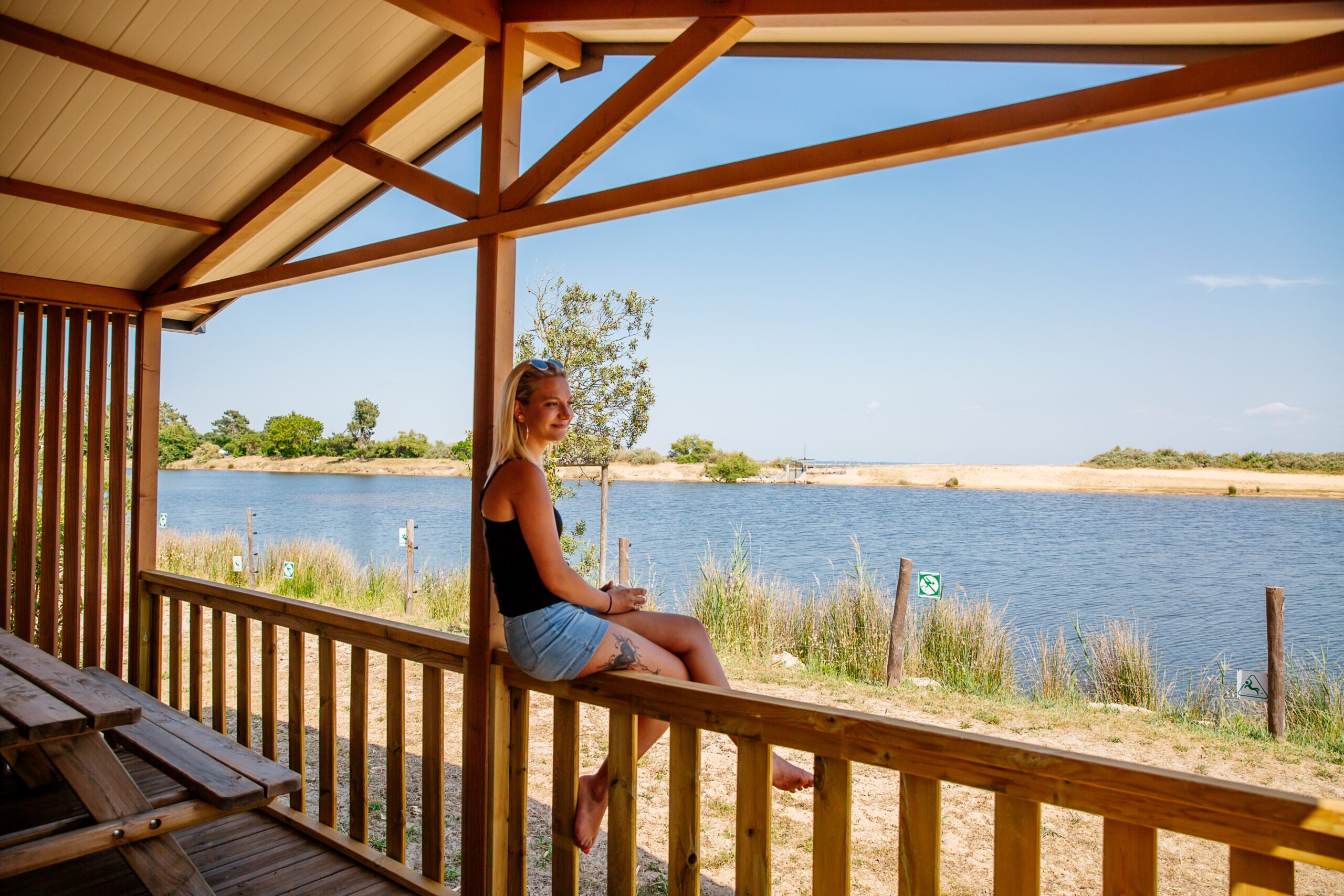 Une femme regarde le Bassin en étant assise sur la rambarde d'une cabane dans le camping des Viviers.