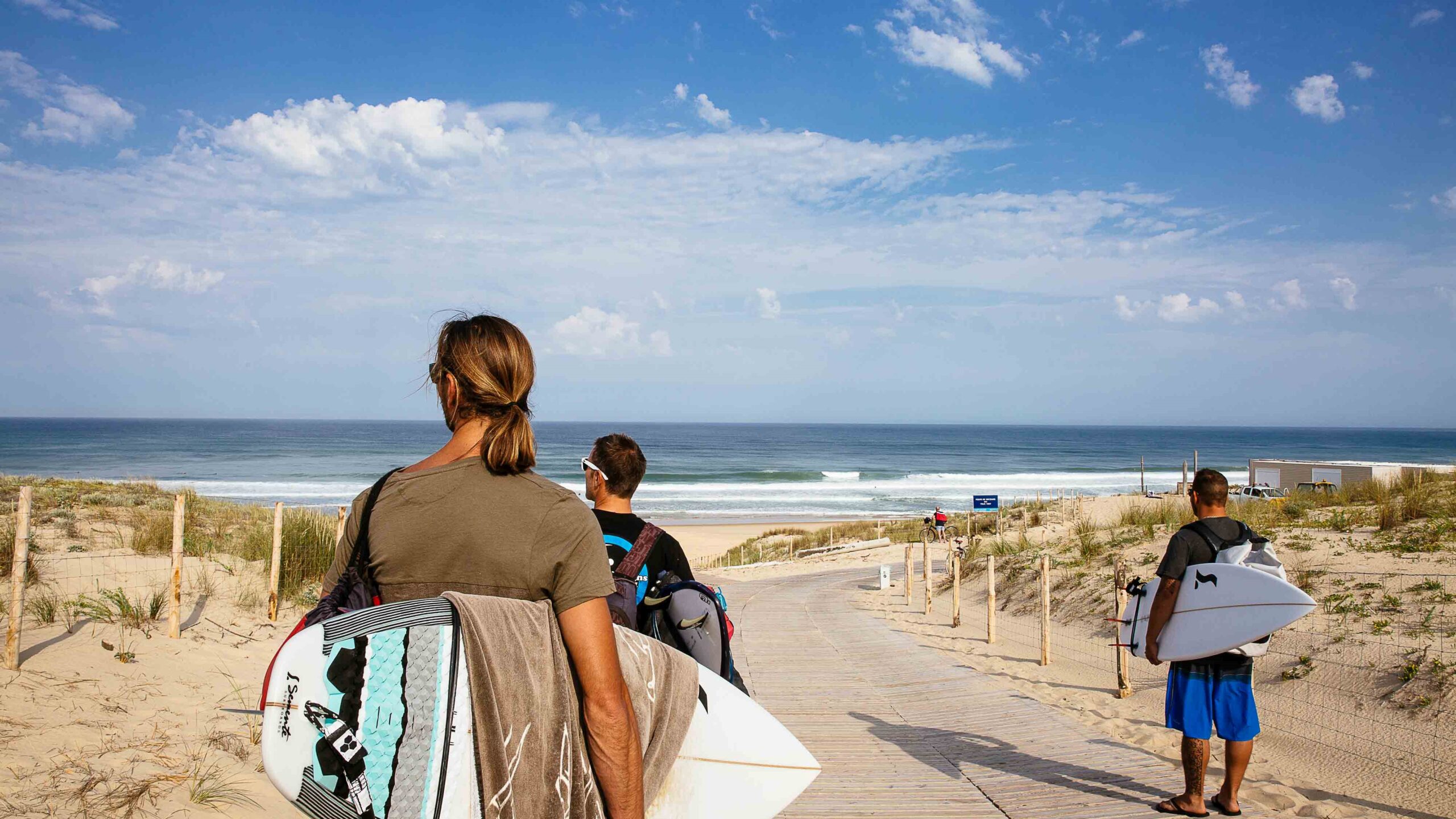 Trois amis marchent ensemble, planches de surf sous le bras, regardant l'océan, prêts à profiter d'une session de surf à l'océan.