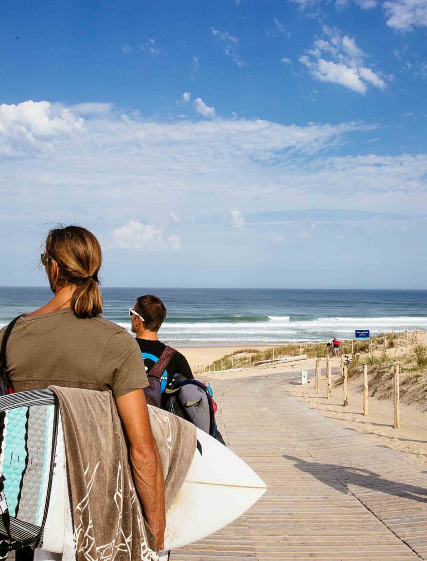 Trois amis marchent ensemble, planches de surf sous le bras, regardant l'océan, prêts à profiter d'une session de surf à l'océan.