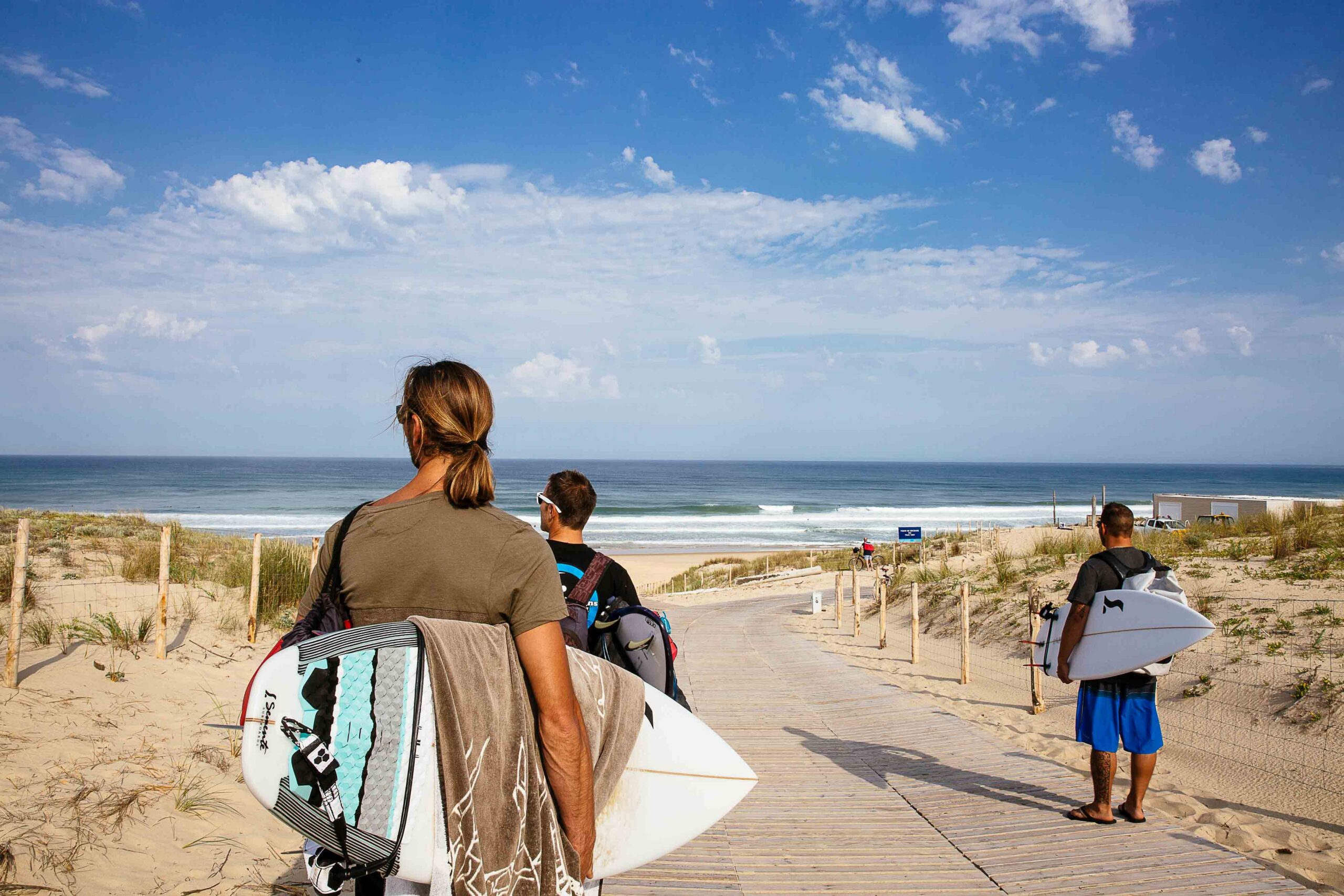Trois amis marchent ensemble, planches de surf sous le bras, regardant l'océan, prêts à profiter d'une session de surf à l'océan.