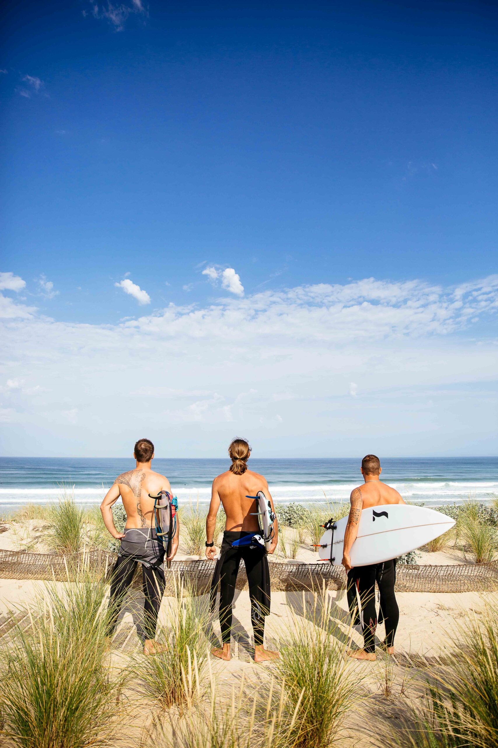 3 surfeurs regardent les conditions planche à la main pour aller à l'eau.