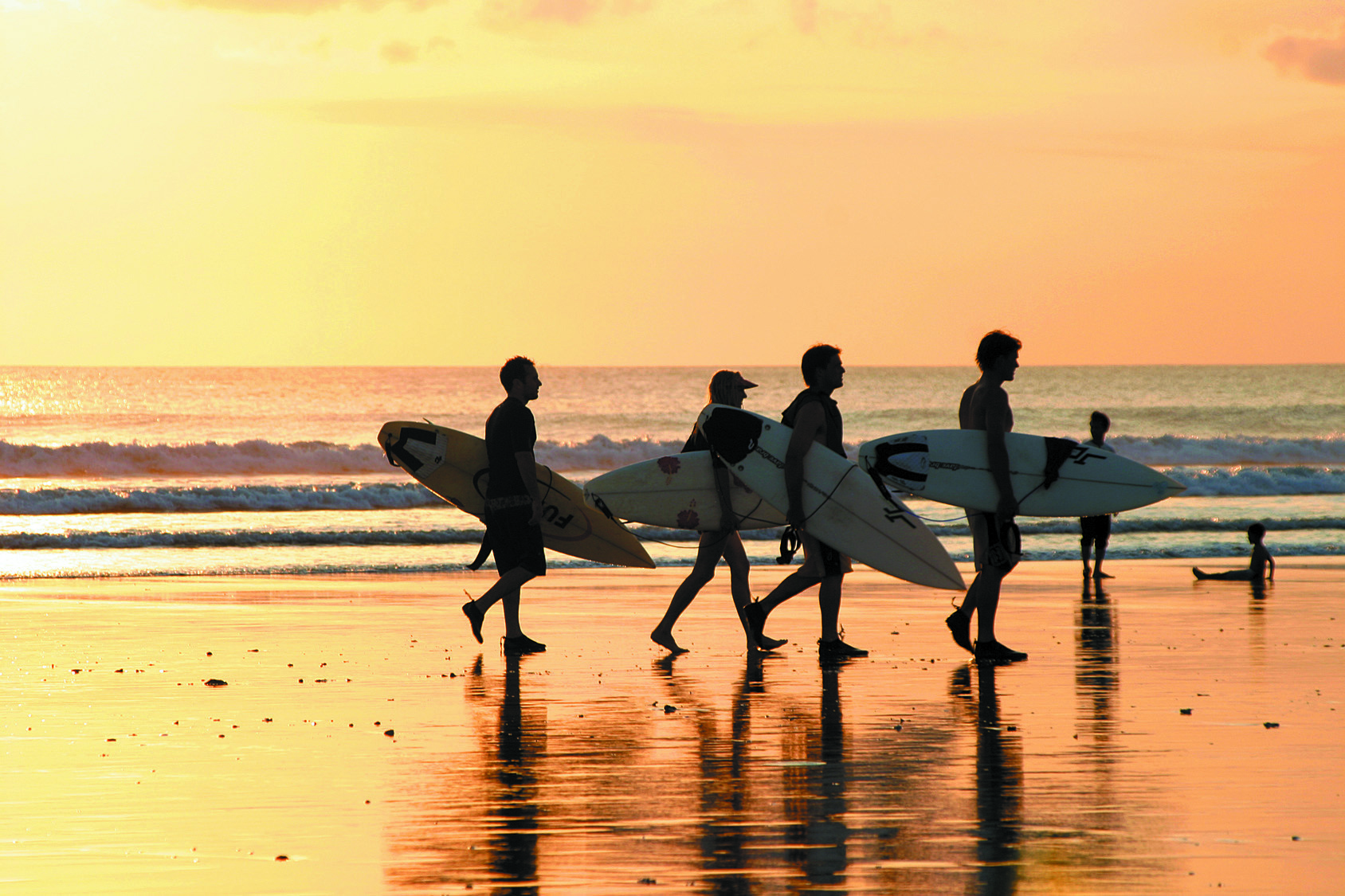 Des surfeurs sortent de l'eau après leur session sous un coucher du soleil.