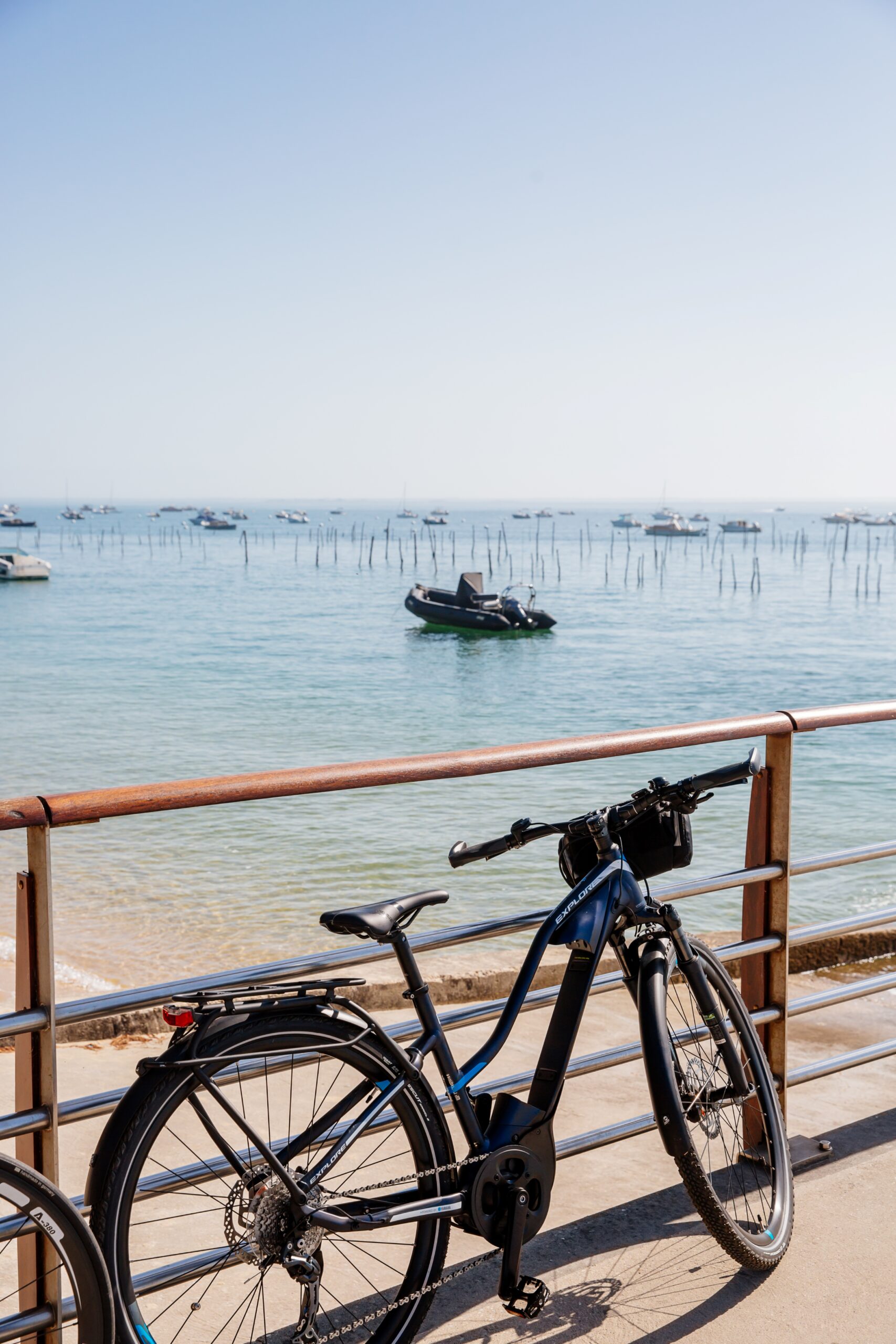 Un vélo posé contre une rambarde, avec le Bassin à marée haute en arrière-plan au Cap Ferret.
