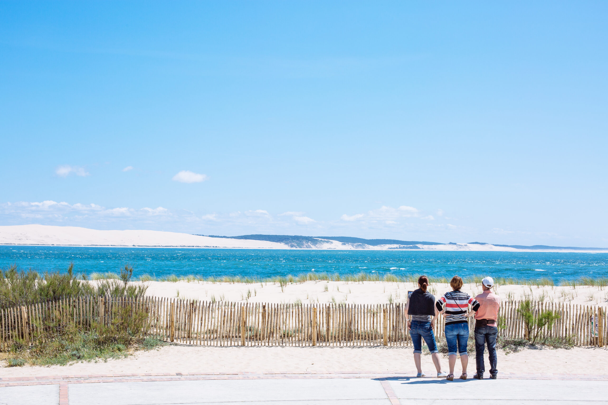3 amis regardent le Bassin au Cap Ferret avec la dune du pilat en arrière plan.