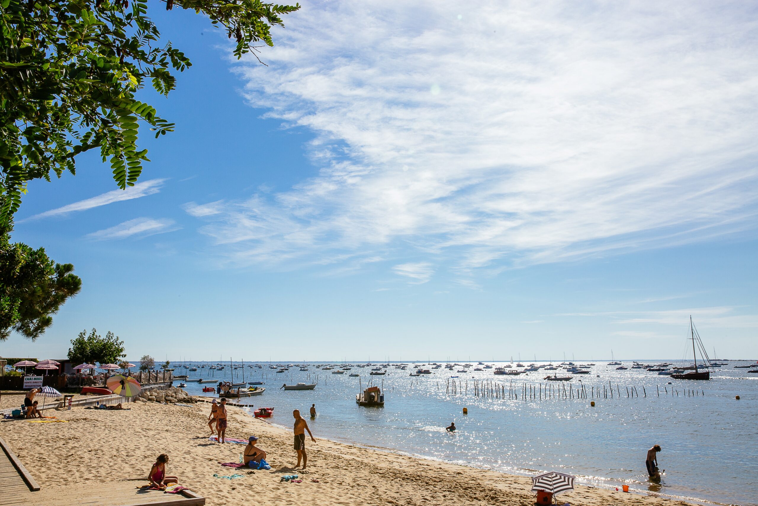 La plage de Grand Piquey en été, avec des baigneurs dans l’eau et d’autres personnes allongées sur leur serviette, profitant du soleil.