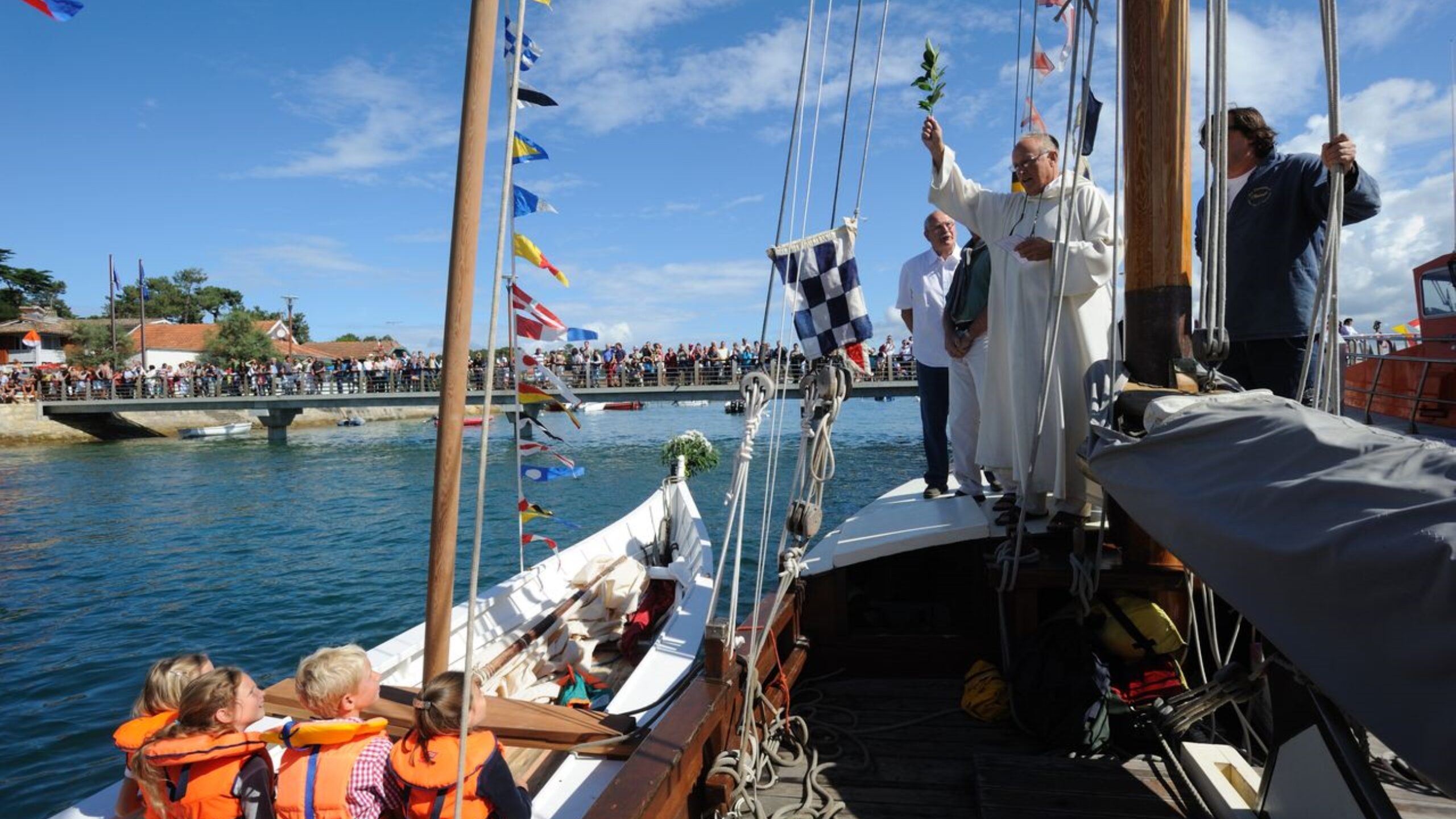 Deux bateaux participent à la fête de la Mer : l'un accueille un prêtre, tandis que l'autre est rempli d'enfants, incarnant l'esprit festif de cette célébration.