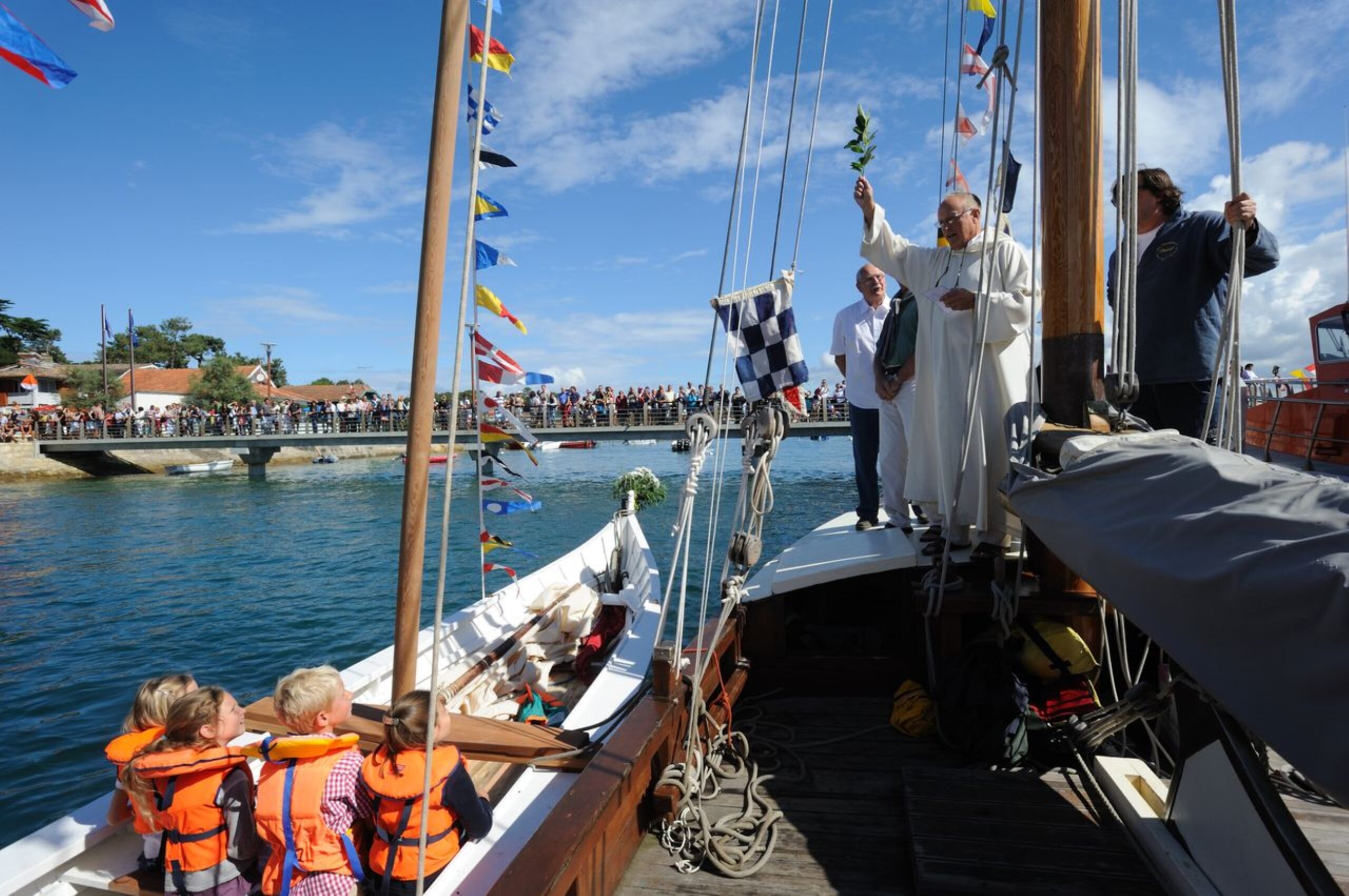 Deux bateaux participent à la fête de la Mer : l'un accueille un prêtre, tandis que l'autre est rempli d'enfants, incarnant l'esprit festif de cette célébration.
