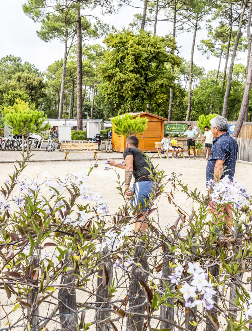Des joueurs en pleine partie de pétanque sur le terrain, concentrés sur leur lancer.