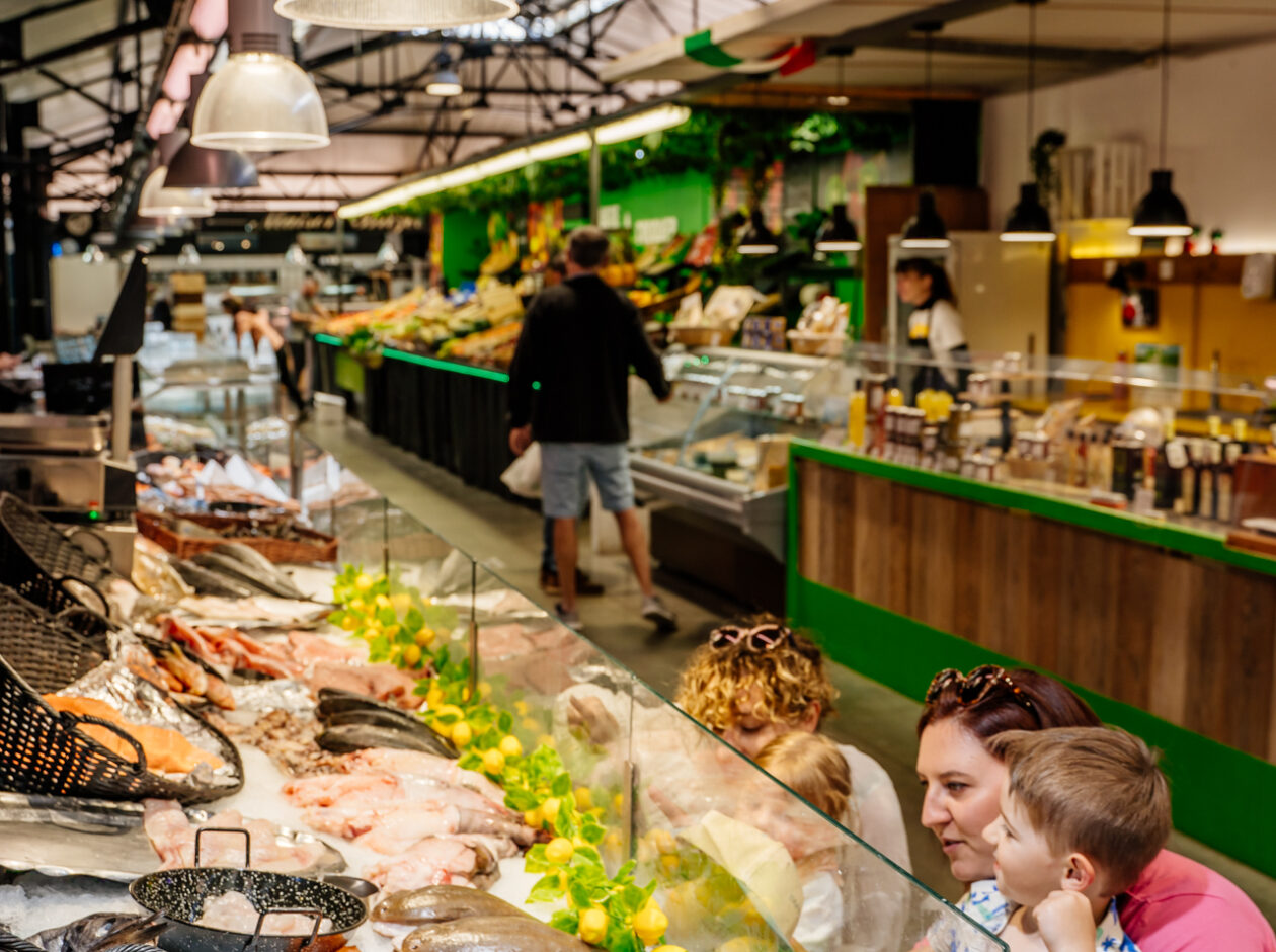 Deux mamans avec leurs jeunes enfants choisissent du poisson frais sur un étal de produits de la mer dans le marché couvert de Claouey à Lège-Cap Ferret, sur le Bassin d’Arcachon.