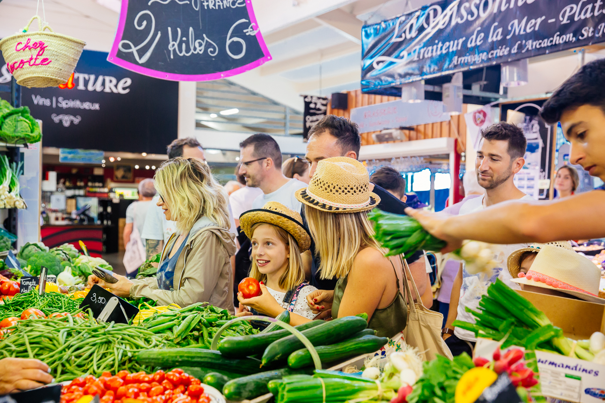 Une famille choisit des fruits et légumes frais sur un stand de producteurs locaux dans le marché couvert de Piraillan à Lège-Cap Ferret, sur le Bassin d’Arcachon.